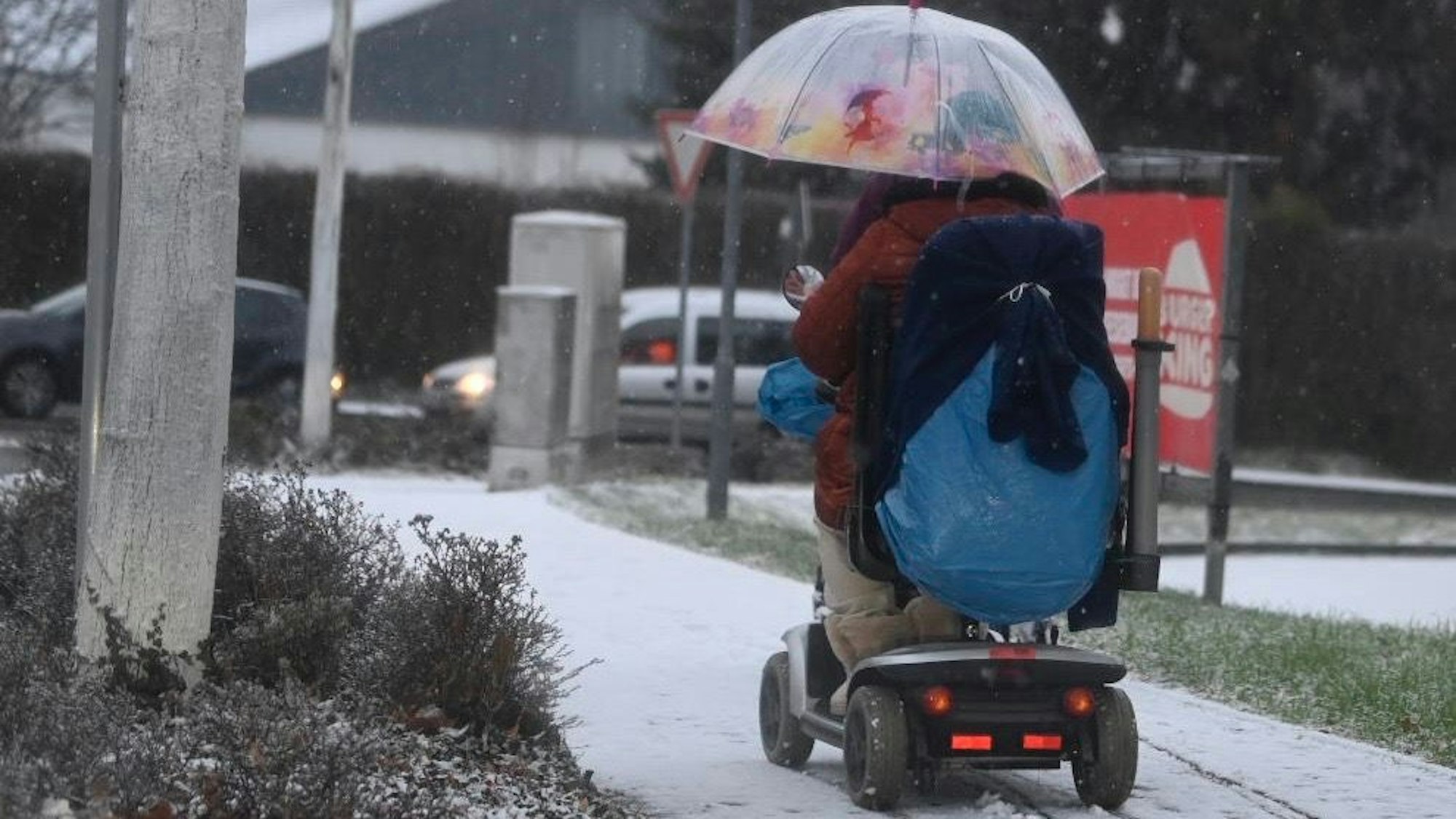 Ein Schirm soll die Seniorin auf dem Elektromobil in Euskirchen vor dem Schnee schützen.