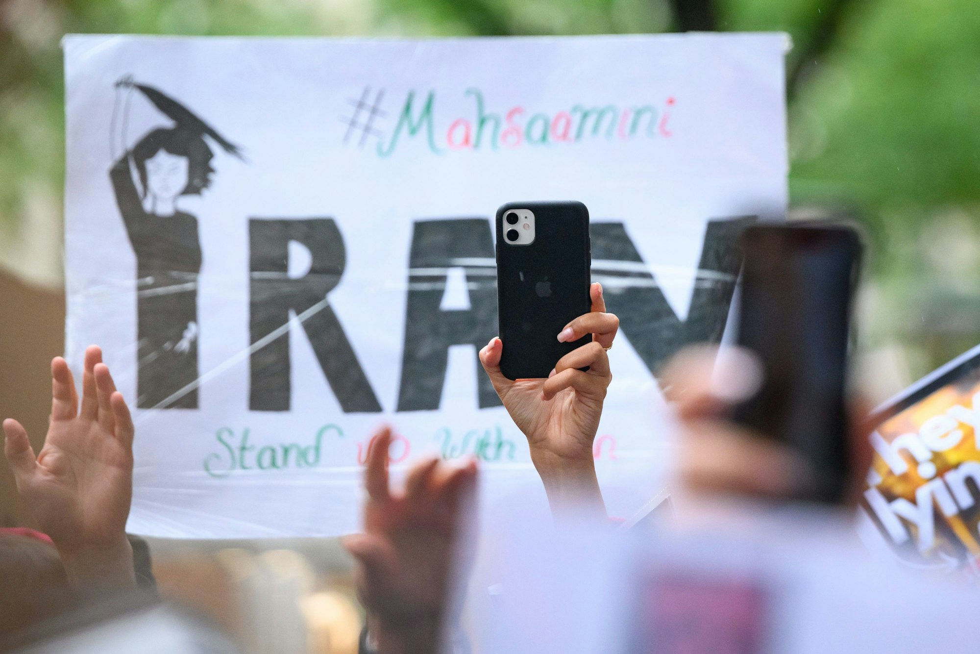 Ein Smartphone wird vor einem Plakat in die Höhe gehalten auf einer Solidaritätskundgebung nach dem Tod von Iranerin Mahsa Amini.