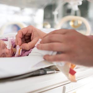 Ein zu früh geborenes Baby liegt im Krankenhaus in einem Inkubator. Eine Pflegekraft hält ihm einen winzigen Schnuller vor den Mund.