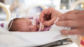 Ein zu früh geborenes Baby liegt im Krankenhaus in einem Inkubator. Eine Pflegekraft hält ihm einen winzigen Schnuller vor den Mund.
