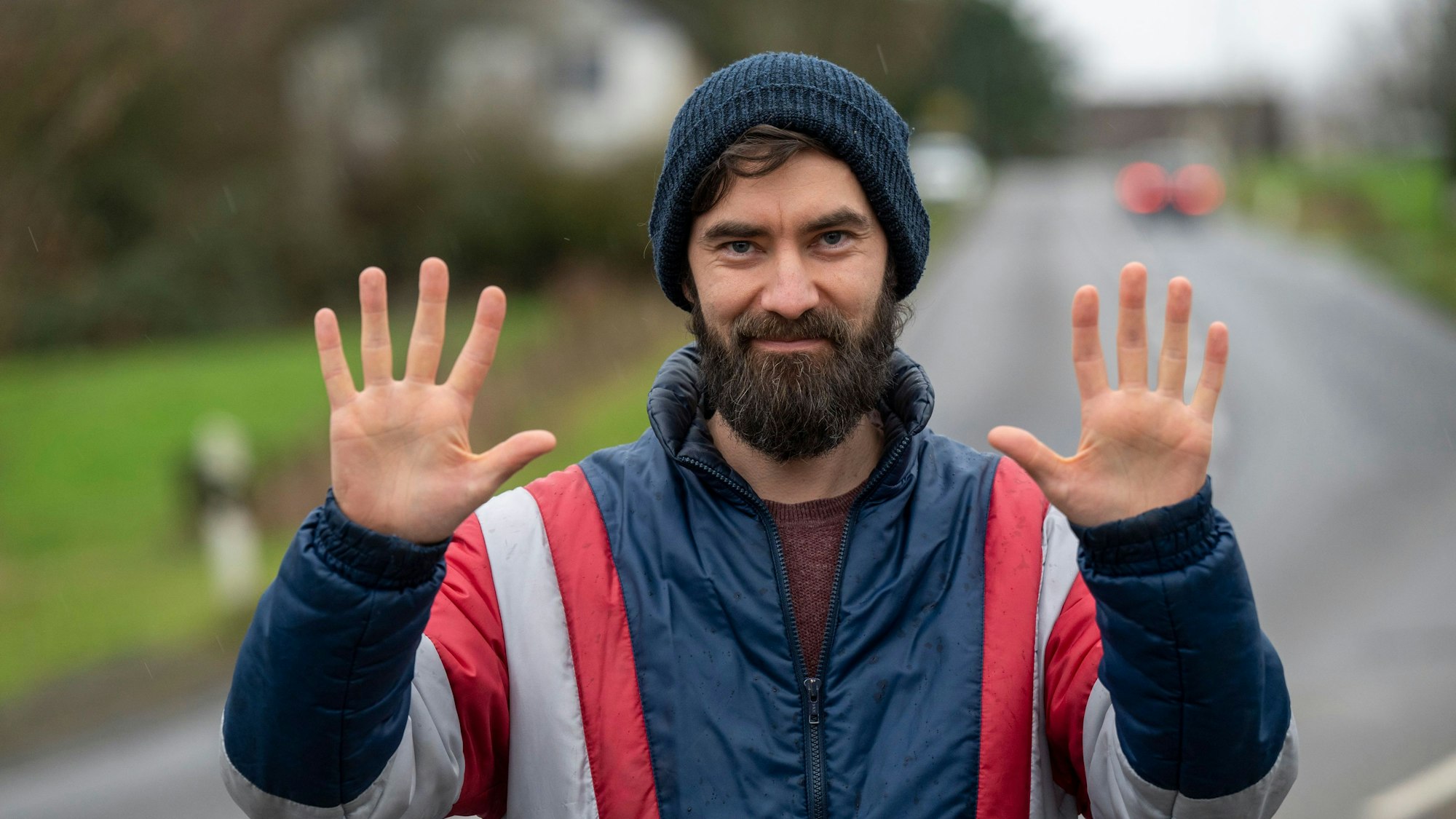 Simon Werle ist Aktivist der „Letzten Generation“. Er steht auf einer Landstraße und hält seine Handinnenflächen nach oben.