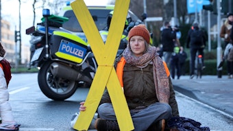 Caroline Schmidt hält bei einer Aktion in Köln eine große, gelbe Pappe in X-Form hoch.