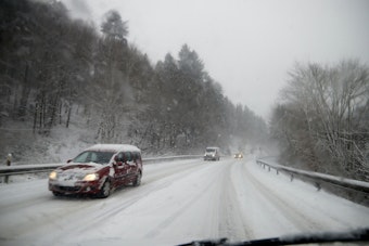 Eine komplett mit Schnee bedeckte Fahrbahn auf einer Straße in der Eifel. Es schneit kräftig.