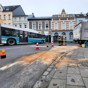 Ein blau-weißer Bus passiert an der Unfallstelle vorbei die Ecke Linzer Straße/Am Saynschen Hof. Mit bräunlichen Bindemitteln haben Feuerwehrleute die ausgelaufenen Betriebsstoffe abgestreut.