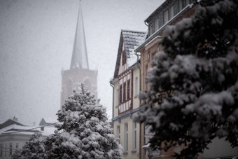 Schneefall in Euskirchen, ein Kirchturm und Häuser sind im Schneetreiben zu sehen.