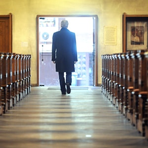 Zu sehen ist ein Mann, der eine Kirche durch den Mittelgang verlässt und Richtung geöffneter Ausgangstür geht.