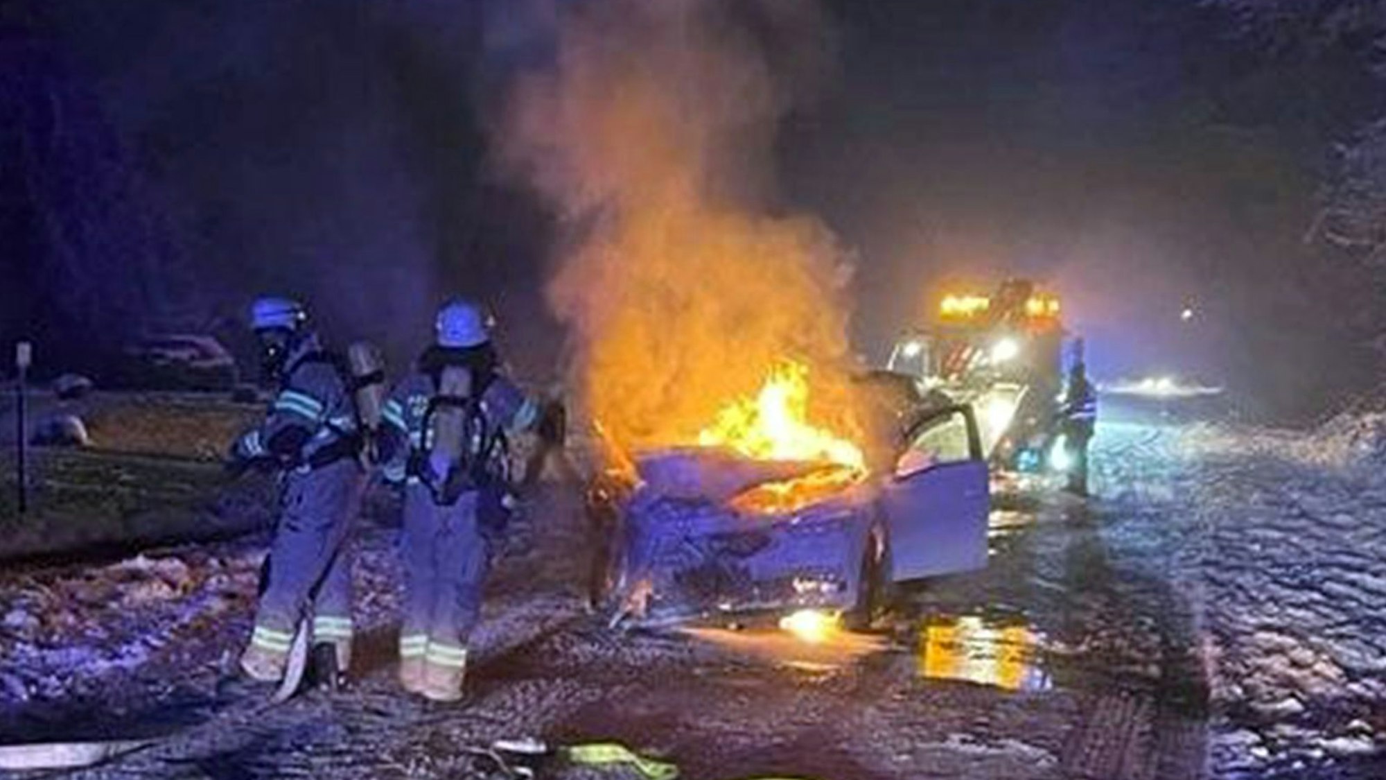 Feuerwehrleute löschen ein brennendes Auto auf einer schneebedeckten Straße.
