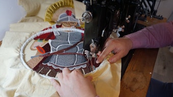 Eine Figur in einer Ritterrüstung wird auf einen hellen Stoff gestickt.