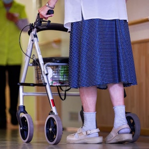 Eine Seniorin geht mit ihrem Rollator über den Gang in einer Pflegeeinrichtung.