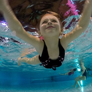 Ein Kind lächelt beim Schwimmen, von Unterwasser fotografiert.