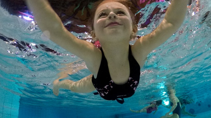 Ein Kind lächelt beim Schwimmen, von Unterwasser fotografiert.