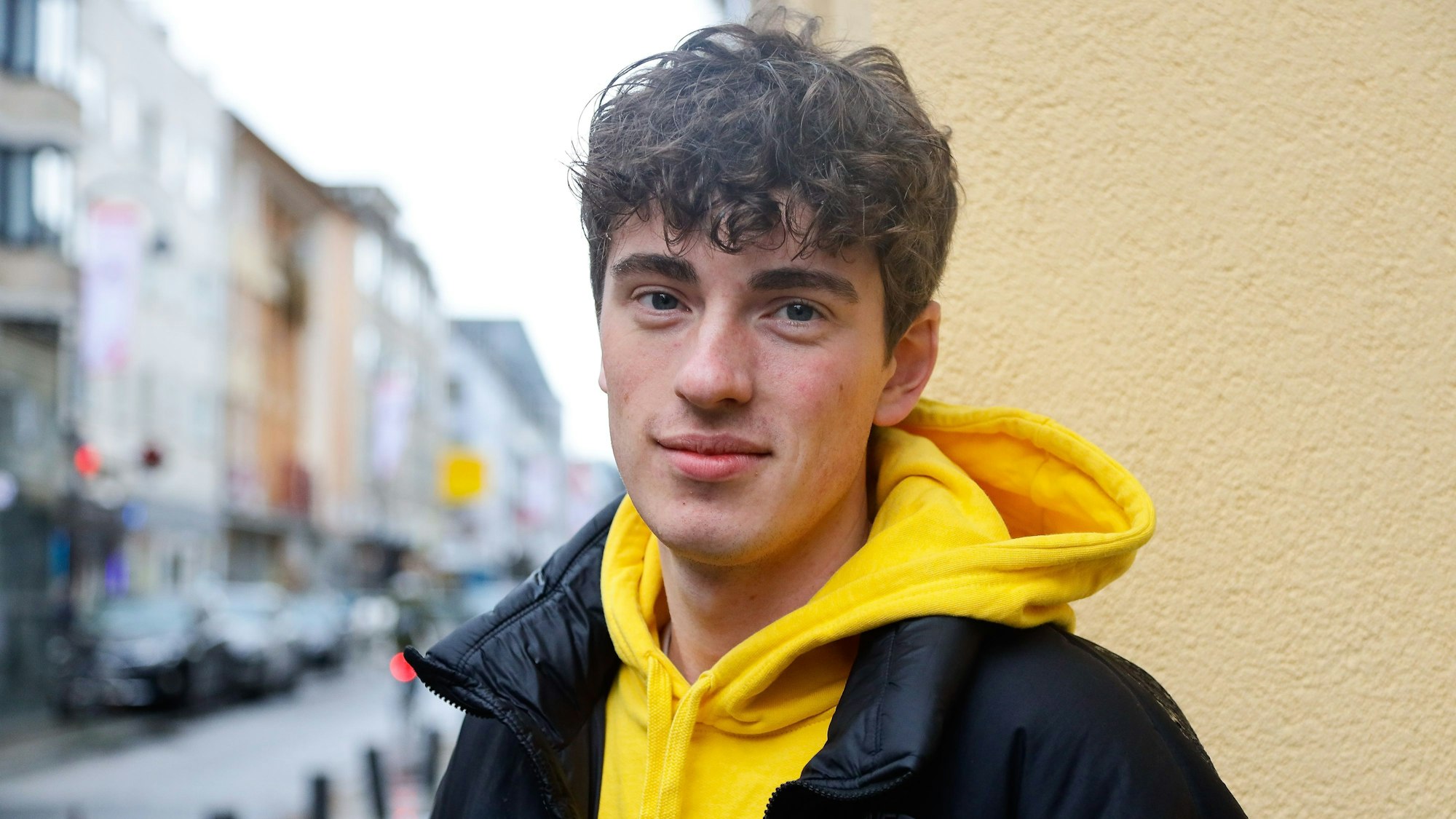 Robin Napiany ist Klima-Aktivist bei der Letzten Generation. Er steht auf der Severinstraße und lächelt in die Kamera.