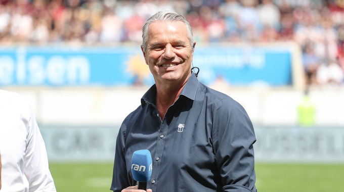 Jan Stecker steht mit einem blauen Mikrofon in der Hand in einem Stadion.