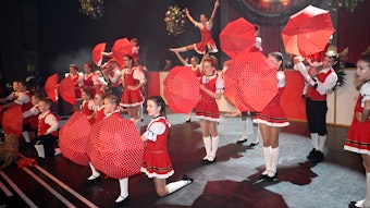 Die Tanzgruppe der Strunde-Pänz steht mit aufgespannten Schirmen auf der Bühne des Bergischen Löwen.