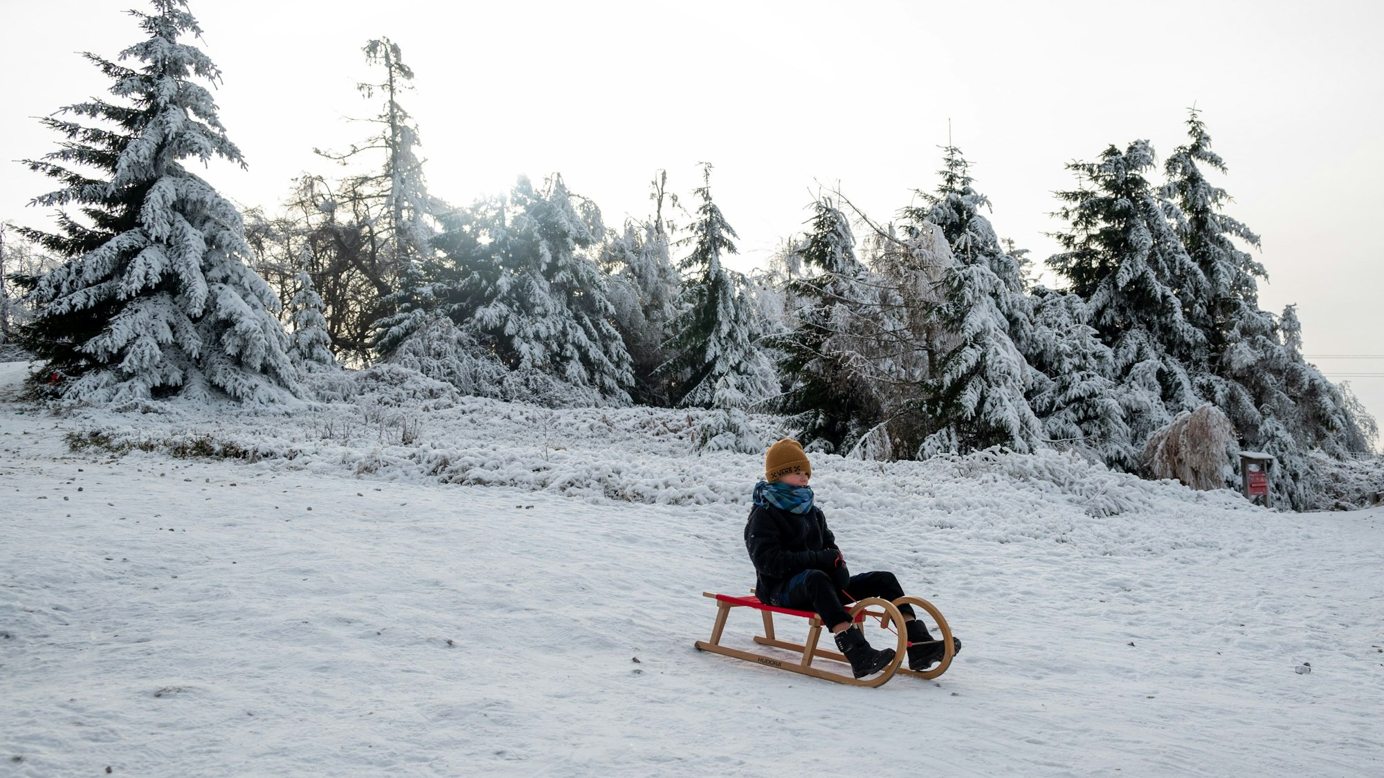 Ein Kind fährt mit einem Schlitten einen zugeschneiten Hang hinunter
