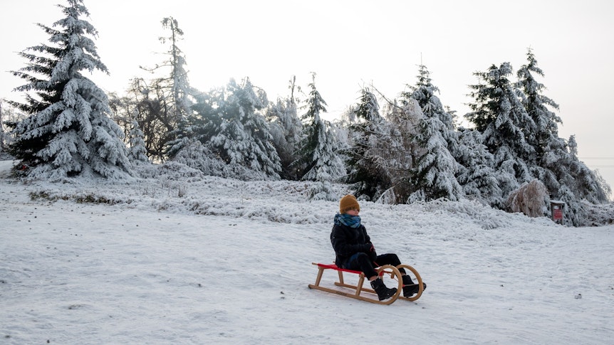 Ein Kind fährt mit einem Schlitten einen zugeschneiten Hang hinunter