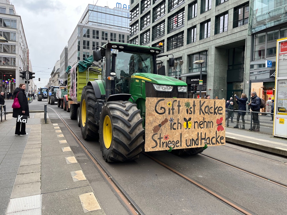 Ein Traktor mit einem Protestplakat fährt durch die noble Berliner Friedrichstraße.