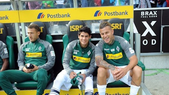 Julio Villalba (M.) sitzt am 9. September 2017 auf der Bank im Borussia-Park zwischen Fabian Johnson (l.) und Raul Bobadilla (r.). Villalba hält ein Trikot von Borussia in der Hand.