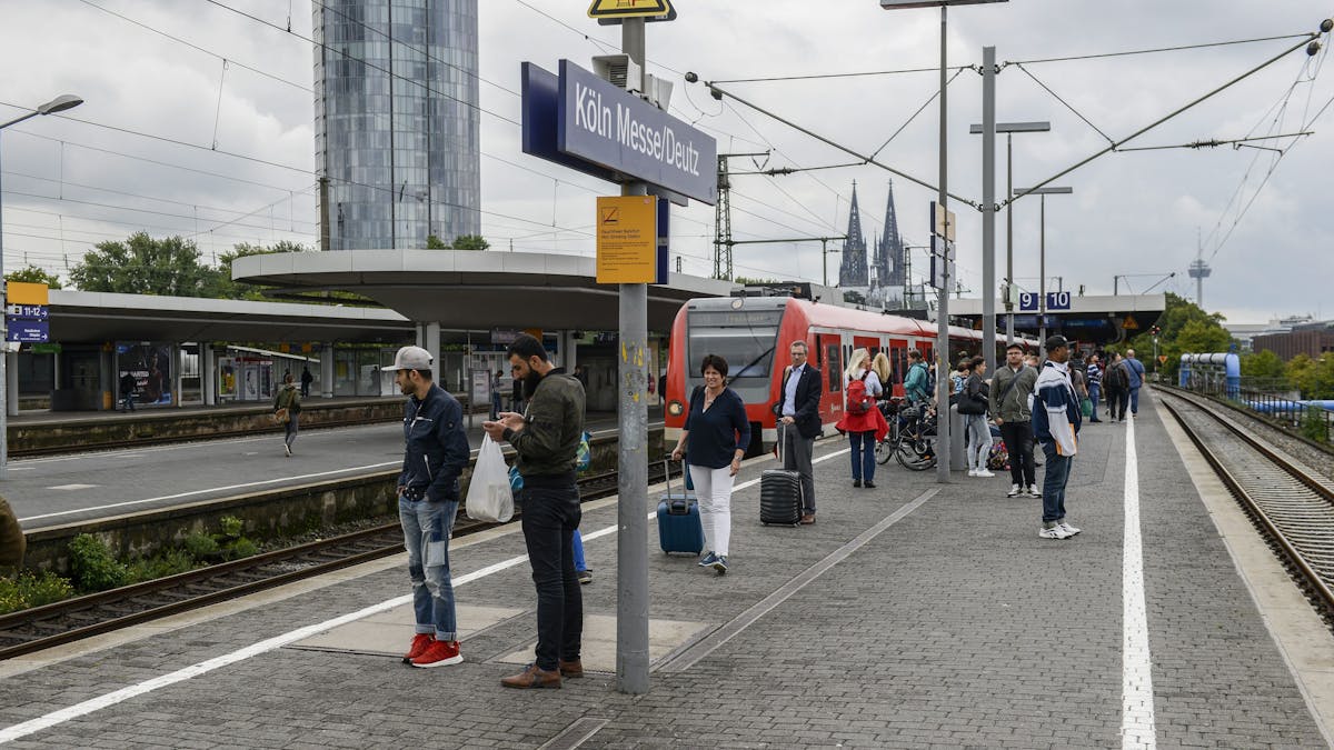 Menschen warten am Bahnsteig in Köln Messe/Deutz auf einen Zug.