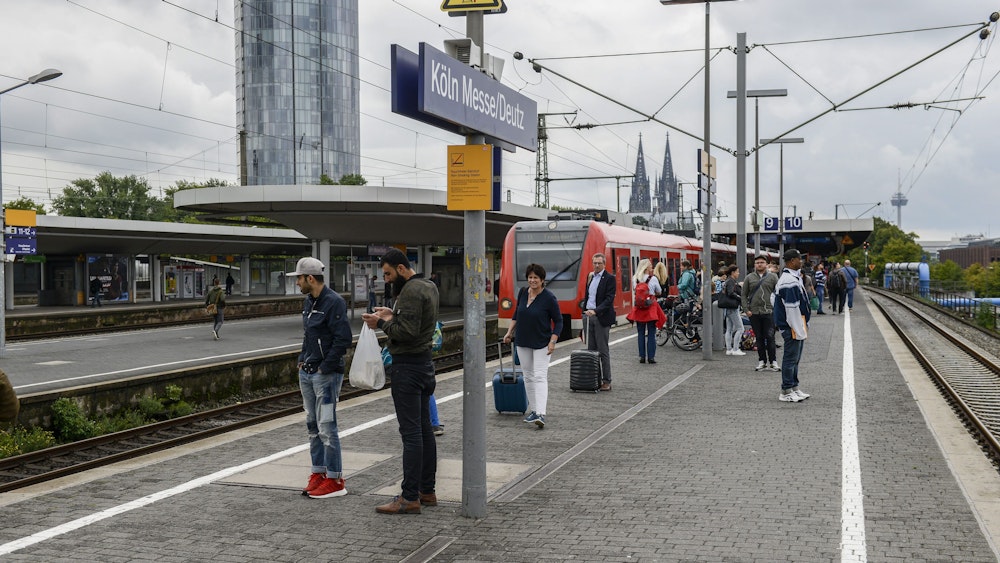 Menschen warten am Bahnsteig in Köln Messe/Deutz auf einen Zug.