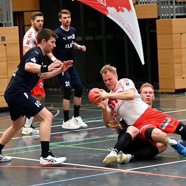 Ein Handballer wird von seinem Gegenspieler auf den Boden gezogen.