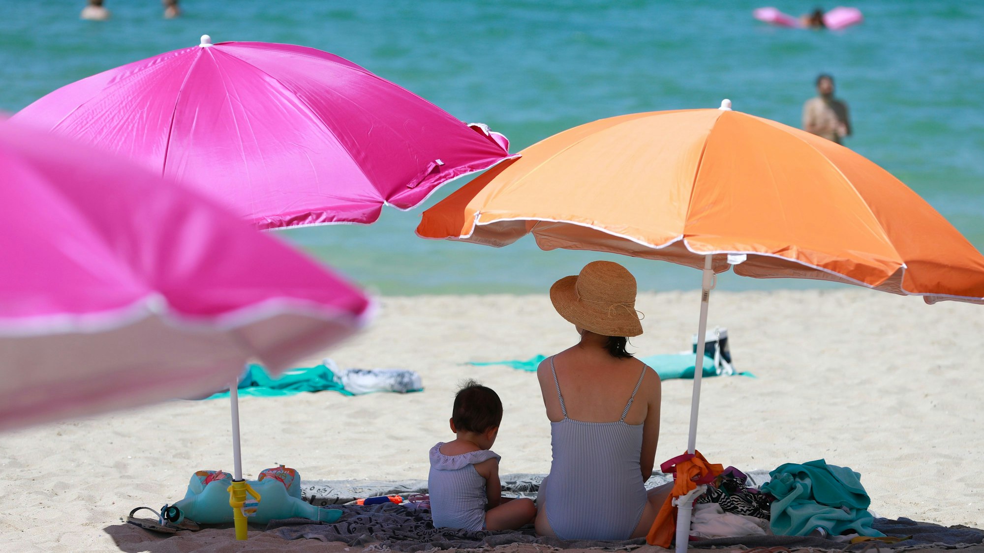 Eine Frau sitzt neben ihrem Kind unter einem Sonnenschirm an einem warmen Sommertag am Strand von Mallorca.