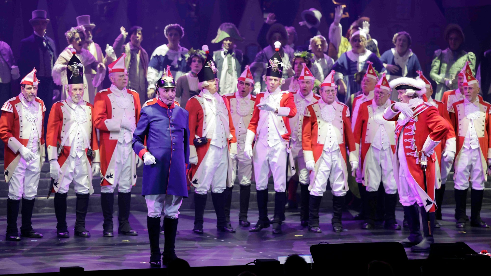 Beim Diverteissementchen stehen viele Männer in rot-weißen Uniformen auf der Bühne, vorne ein "Preuße" in blau-roter Uniform.