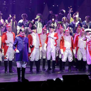 Beim Diverteissementchen stehen viele Männer in rot-weißen Uniformen auf der Bühne, vorne ein "Preuße" in blau-roter Uniform.