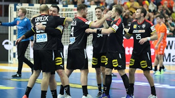 Deutsche Handballspieler, in schwarzen Trikots, freuen sich nach Spielende und liegen sich in den Armen.