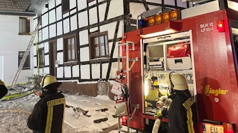 Ein Feuerwehrfahrzeug und Feuerwehrleute stehen vor einem Fachwerkhaus.