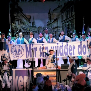 Blau-weiß kostümierte Altstadtfunken mit einem Transparent „Mir sin widder do“ auf der Bühne