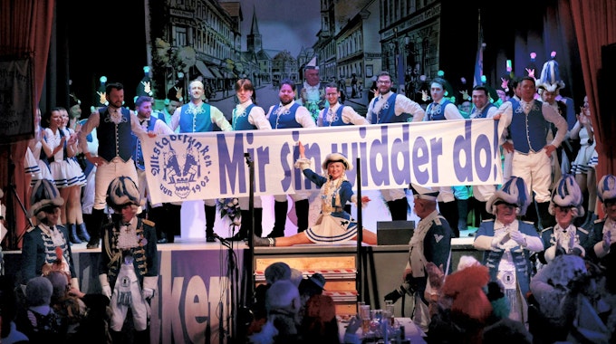 Blau-weiß kostümierte Altstadtfunken mit einem Transparent „Mir sin widder do“ auf der Bühne