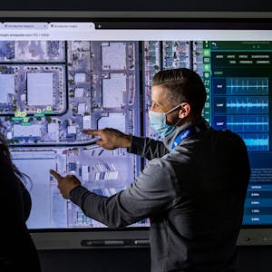 Vor einem großen Monitor mit einer Luftaufnahme von Las Vegas stehen eine Frau und ein Mann. Der Mann deutet auf Stellen auf dem Foto.