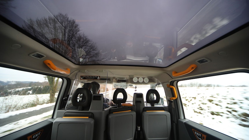 Drei der sechs Sitzplätze sind auf dem Bild aus dem Inneren des „Efi“-Taxis zu sehen. Draußen „fliegt“ eine Landschaft vorbei.