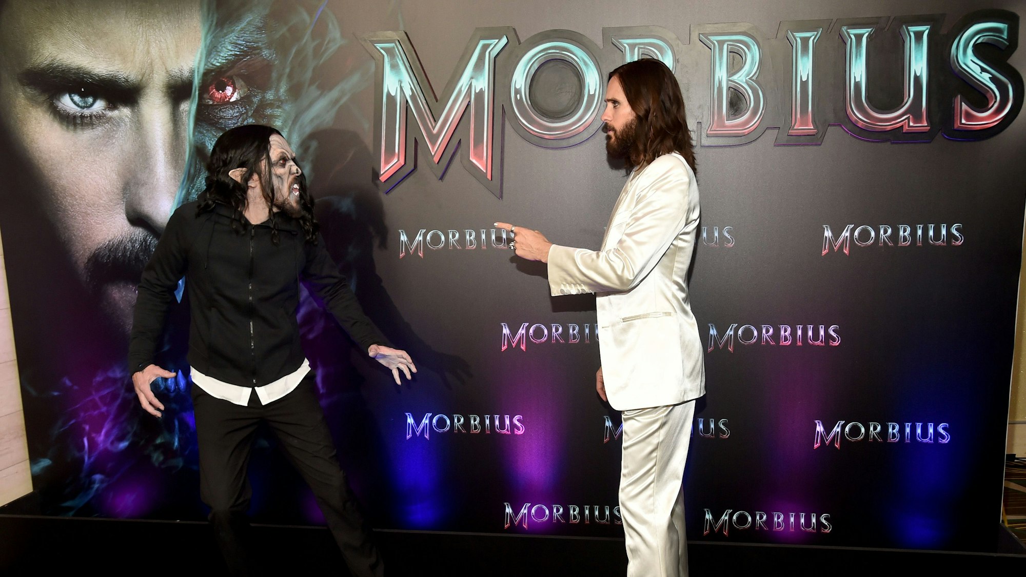 Jared Leto mit Vampir vor einem Filmplakat von „Morbius“.
