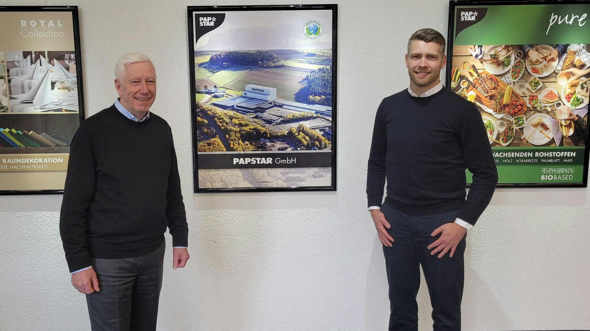 Vor einer Wand mit Fotos stehen die Geschäftsführer von Papstar, Bert Kantelberg und sein Sohn Tom.
