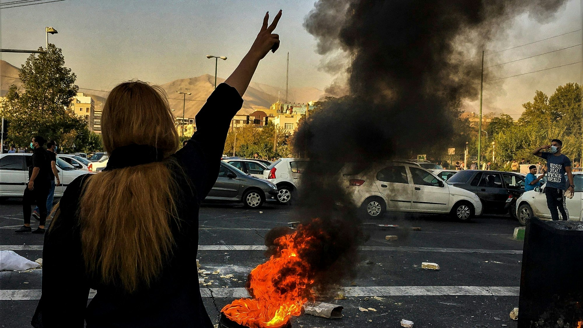 Eine Frau steht während einer Demonstration vor einem brennenden Autoreifen und macht das Victory-Zeichen.