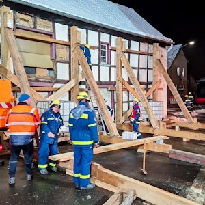 Das THW und die Feuerwehr sichern in Füssenich ein altes Fachwerkhaus. Dazu stellen die Spezialisten in der Dämmerung schwere Holzbalken auf.