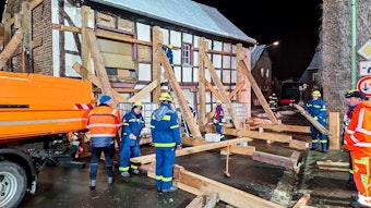 Das THW und die Feuerwehr sichern in Füssenich ein altes Fachwerkhaus. Dazu stellen die Spezialisten in der Dämmerung schwere Holzbalken auf.