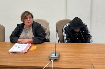 Mit Kapuze im Gesicht sitzt der Angeklagte neben seiner Verteidigerin im Gerichtssaal.