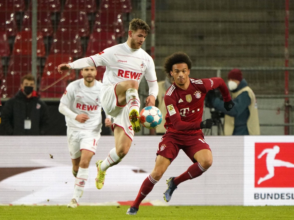 FC-Profi Jan Thielmann (l.) versucht in Bedrängnis von Bayern-Star Leroy Sane einen Ball in der Luft mit Fuß anzunehmen.