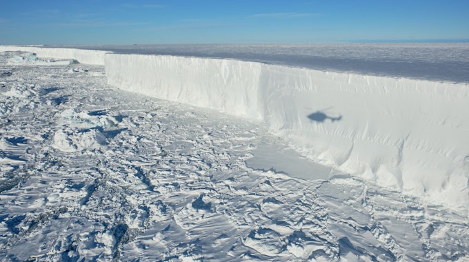 Das Foto zeigt den Eisberg A 74, der sich vom Festland löst, ein Helikopter fliegt darüber.