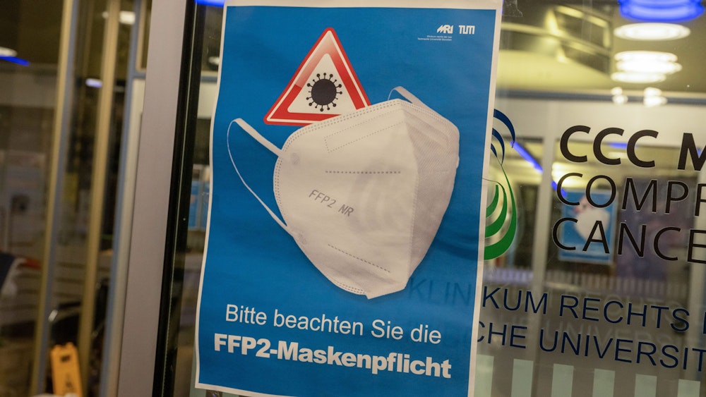 Ein Plakat mit der Aufschrift „Bitte beachten Sie die FFP2-Maskenpflicht“ hängt am Eingang eines Krankenhauses (Symbolbild).
