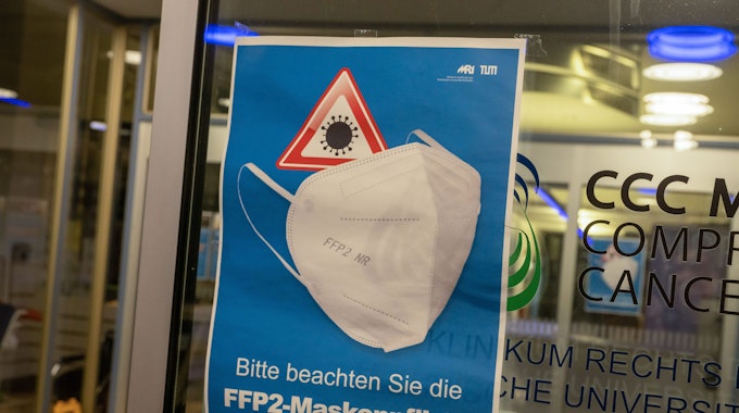 Ein Plakat mit der Aufschrift „Bitte beachten Sie die FFP2-Maskenpflicht“ hängt am Eingang eines Krankenhauses (Symbolbild).