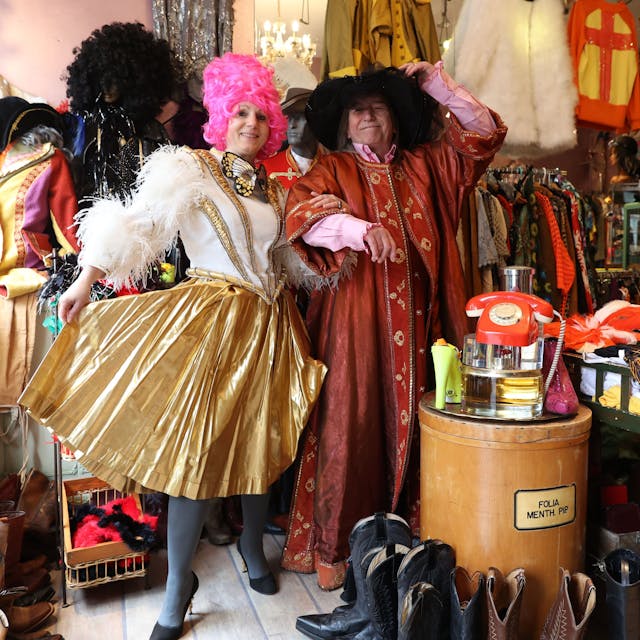 Eine Fau in einem gold-weißen Fransen-Dress und ein Mann in einer rot-goldenen Robe schunkeln in dem dem Second-Hand-Geschäft.