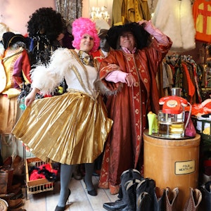 Eine Fau in einem gold-weißen Fransen-Dress und ein Mann in einer rot-goldenen Robe schunkeln in dem dem Second-Hand-Geschäft.
