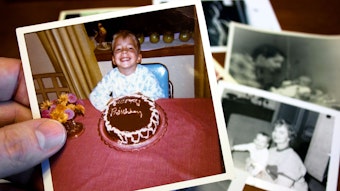Eine Hand hält ein Foto, auf dem ein Junge vor einem Geburtstagskuchen sitzt.