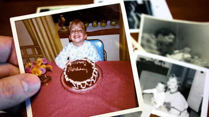 Eine Hand hält ein Foto, auf dem ein Junge vor einem Geburtstagskuchen sitzt.