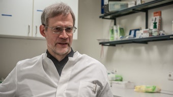 Martin Oehler in weißem Arztkittel mit Stiften in der Brusttasche in einem Behandlungszimmer oder Labor.
