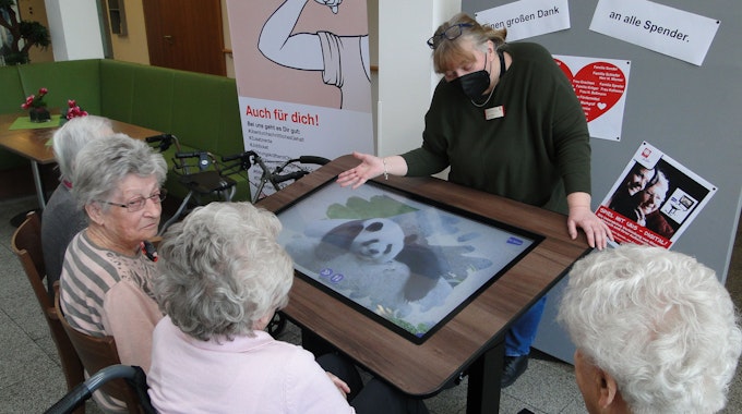 Der neue digitale Spieletisch mit vier älteren Frauen davor sitzend und einer Pflegerin dahinterstehend.
